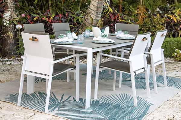 Contemporary outdoor dining furniture set featuring a sleek white table and comfortable grey chairs on a stylish palm leaf rug, ideal for modern patio decor.