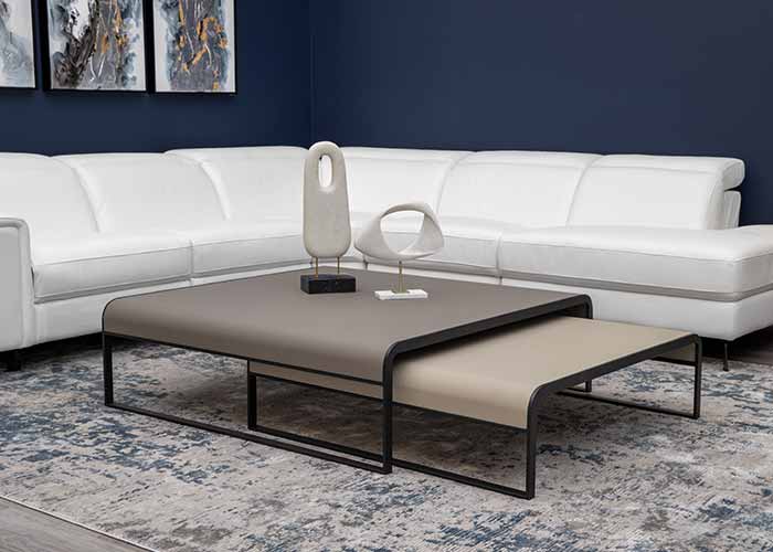 The Galina coffee table, featuring a sleek two-toned design with a beige under-shelf, set against a plush white sofa and dark blue wall.