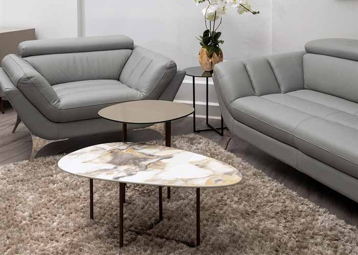The Ginni coffee table, showcasing a round marble top and brass legs, paired with grey modern sofas in a cozy living room setting.