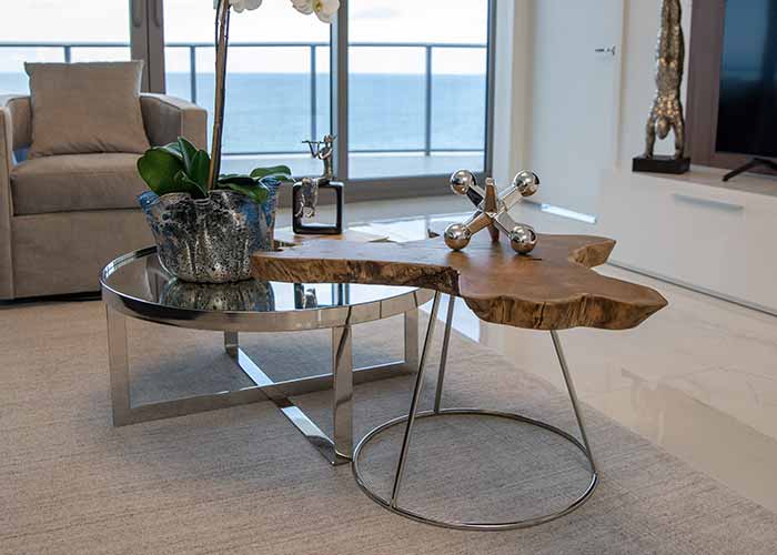 The Varzi coffee table showcases a contemporary aesthetic with its stylish wooden surface and metallic base in a chic, well-lit room.