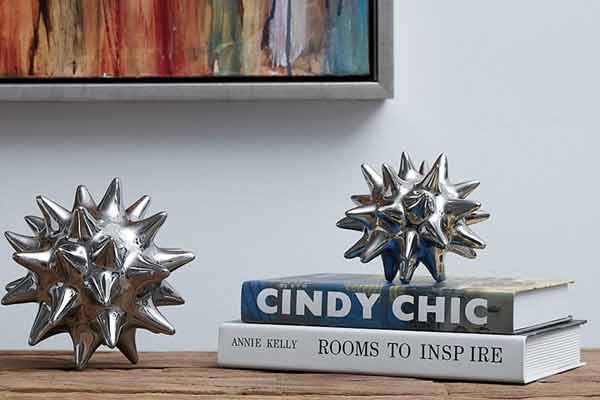 Unique urchin-inspired modern decor pieces in metallic finish, displayed beside books on a wooden shelf, contributing to a trendy and artistic vibe.